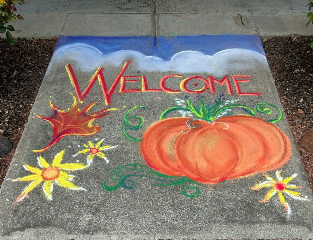 Sidewalk chalk art with pumpkin, flowers, and the word Welcome